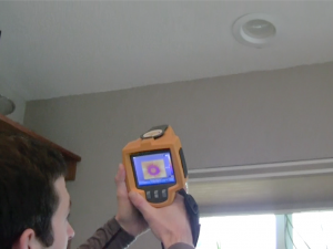 A staff member looks at an infrared camera pointed at a can light on the ceiling of a home.