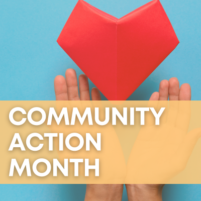 Two hands frame a large, red origami heart over a sky-blue background. A peach-colored banner says "Community Action Month."