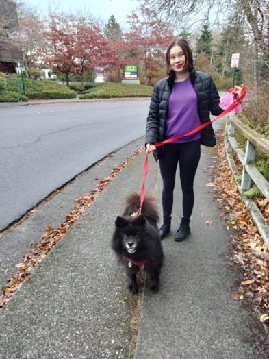 A volunteer smiles while holding the leash of an eager, fluffy black dog.