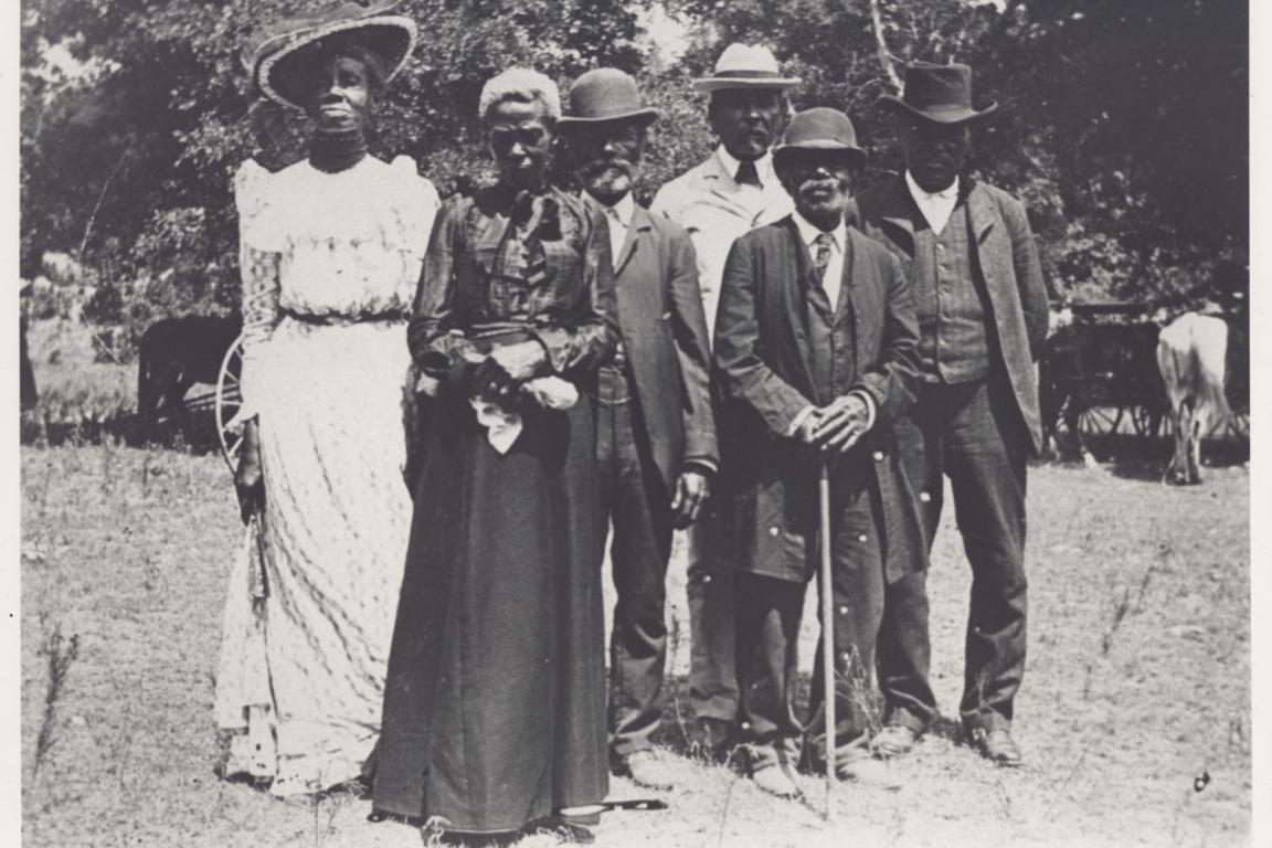 An old black-and-white photograph shows two Black women and four Black men pose, dressed formally for celebration.