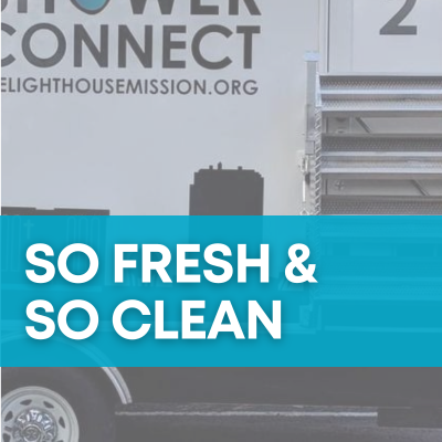 Part of a white truck that says "Shower Connect," which has a raindrop as the 'O'. Below the lettering it says "Thelighthousemission.org." Over top, there is a blue banner with white text on top that says "So Fresh & So Clean."