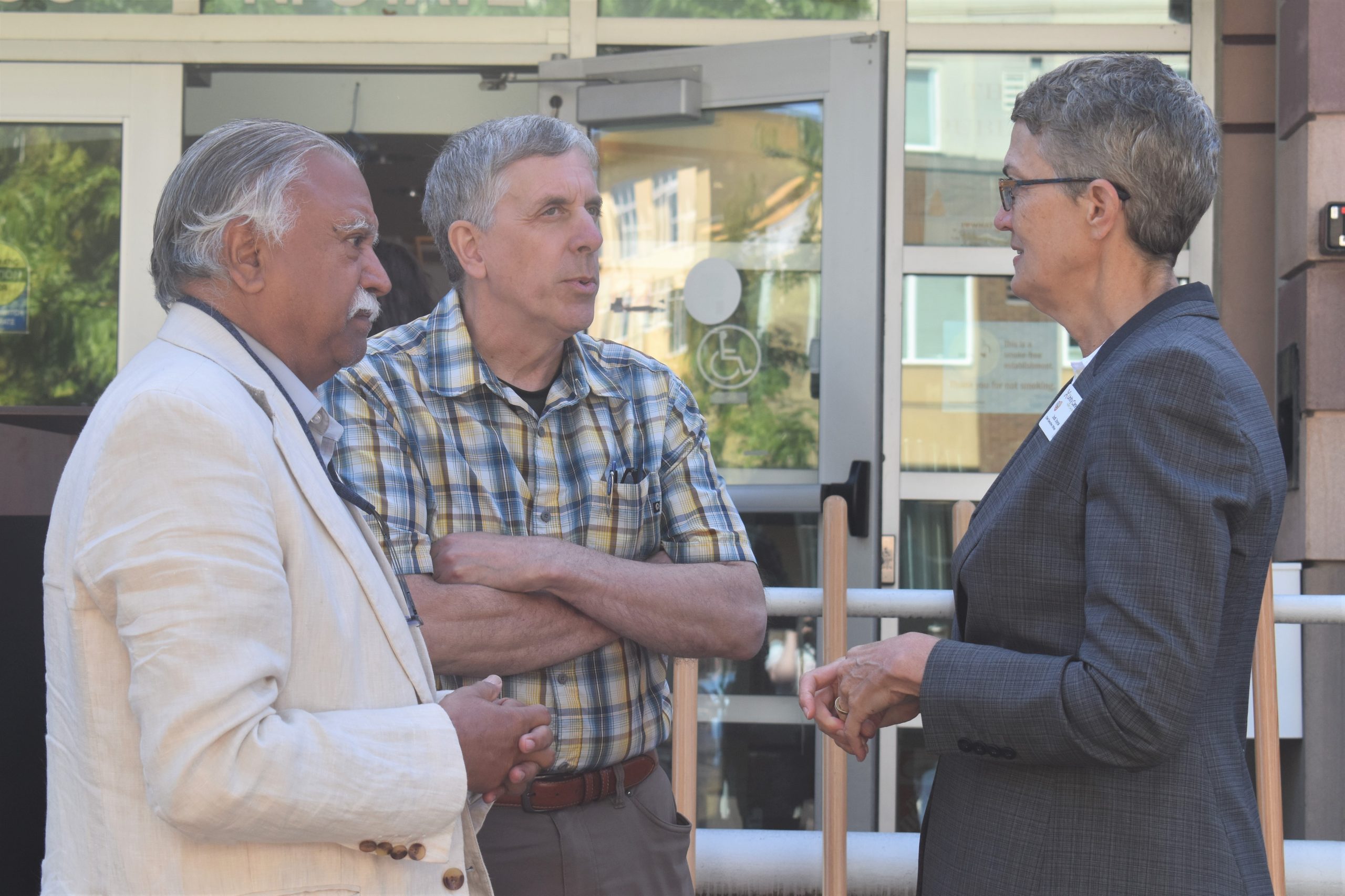 Two men and a woman, all clad in business wear, stand by the door of a building chatting. From left are Satpal Sidhu, Greg Winter, and Jodi Joyce.