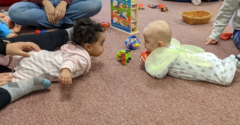 Two babies play together on the floor.