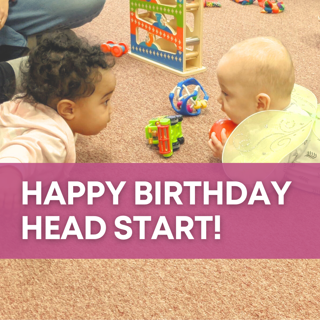 Two babies in onesies play with toys on the floor while looking at each other, one wearing yellow fairy wings. Over the photo is a magenta banner that says "Happy Birthday Head Start" in white text.