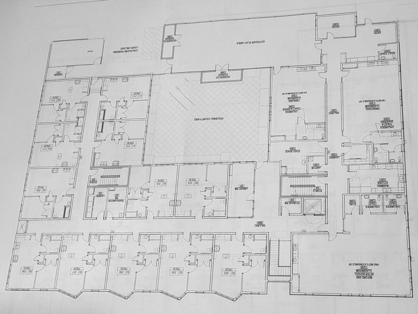 An architectural drawing shows the floor plan of an apartment building that includes a courtyard and library, as well as having a separate child care center on the property that includes an outdoor play area.