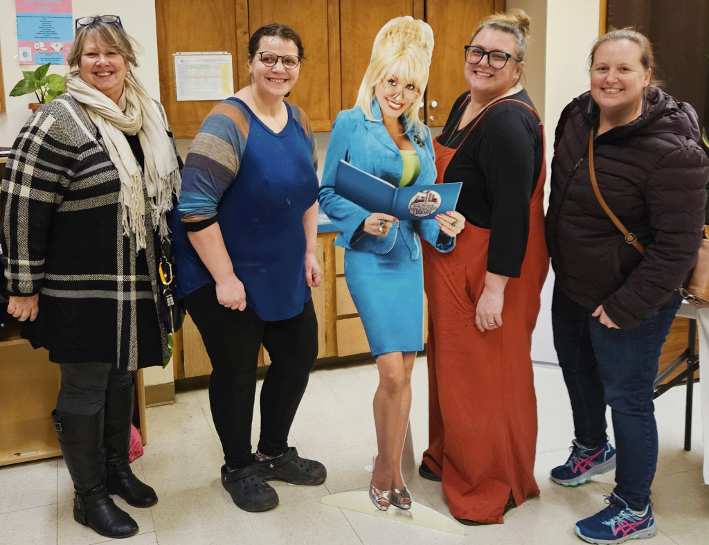 Four women smile together with a life-sized cutout of Dolly Parton.