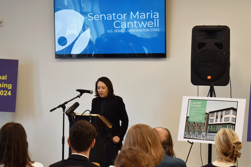 A woman (U.S. Senator Maria Cantwell) speaks at a podium, addressing a group of people.