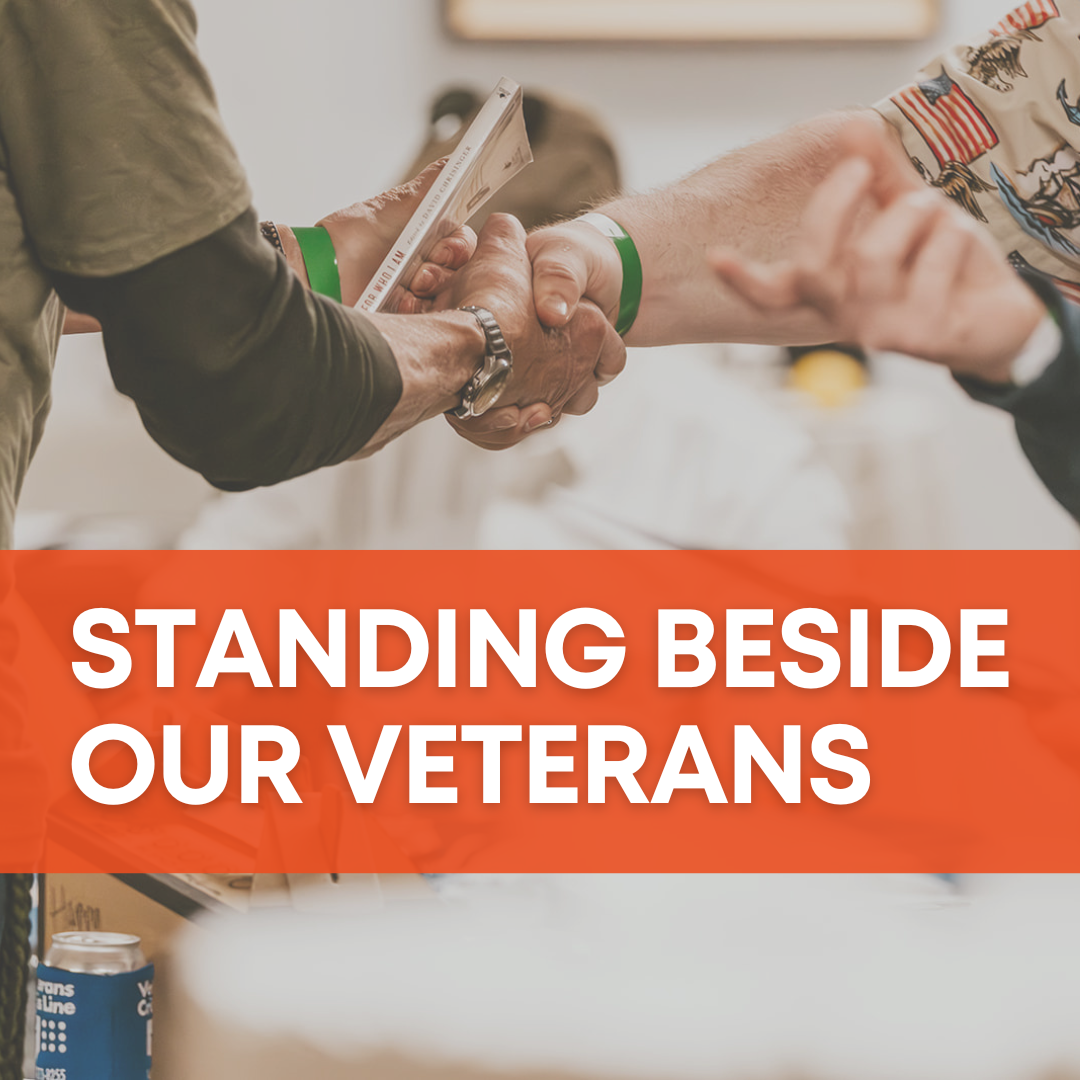 Photo of two people shaking hands with a red-orange banner that says "Standing beside our Veterans"