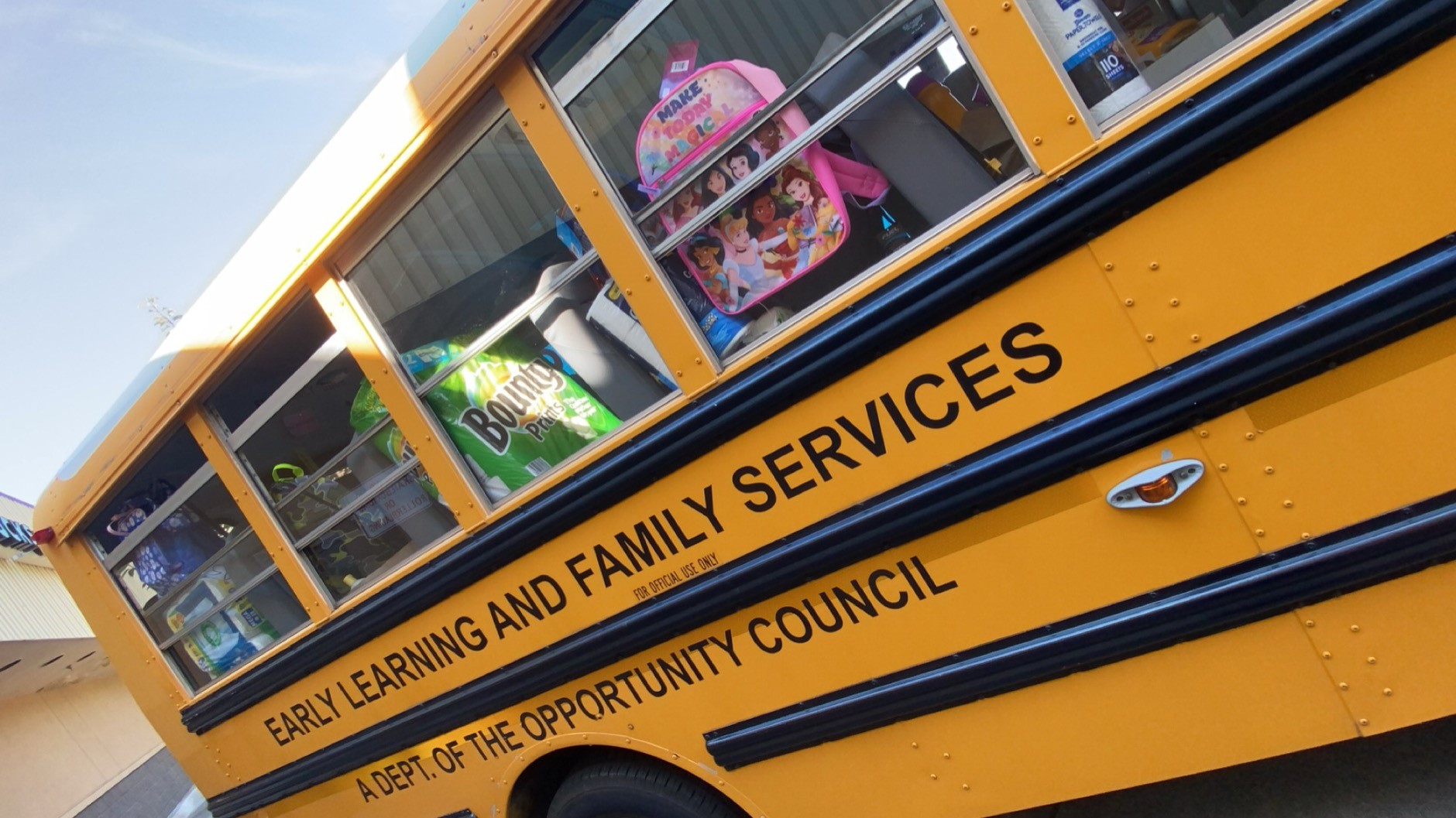 An orange school bus that says "Early Learning and Family Services: a dept. of The Opportunity Council" is filled with household and school supplies.