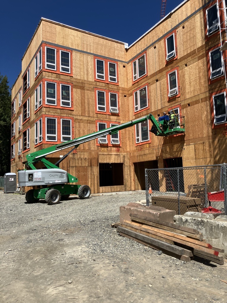 A forklift lifts a person to a window of a building under construction.