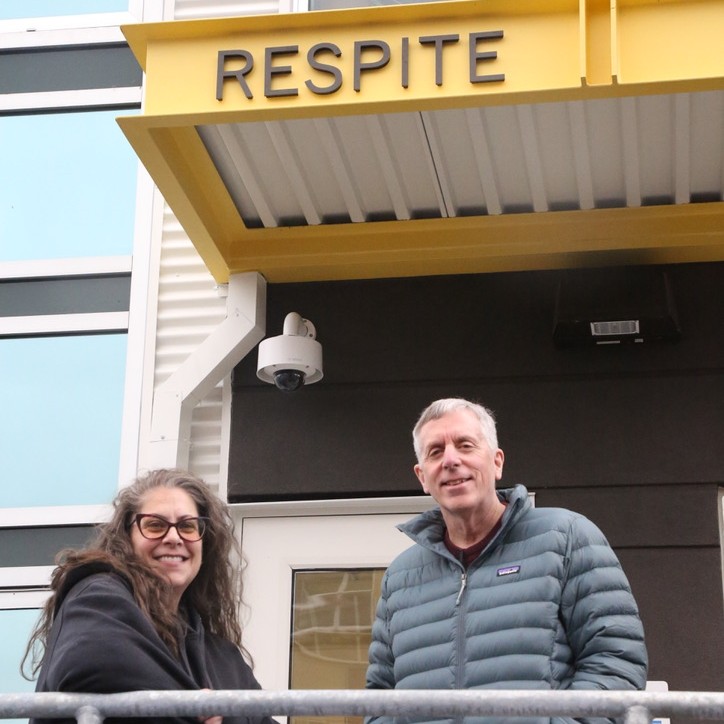 Two people, Marisa Schoeppach and Greg Winter, stand under an awning that says "Respite."