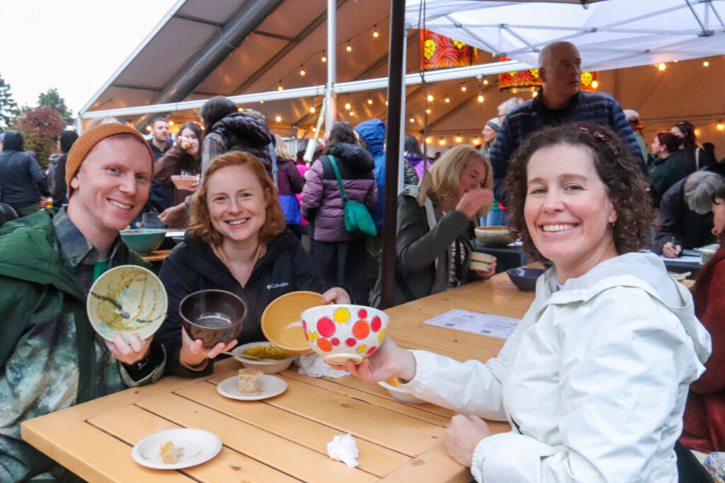 People smiling at a table while holding handmade bowls.