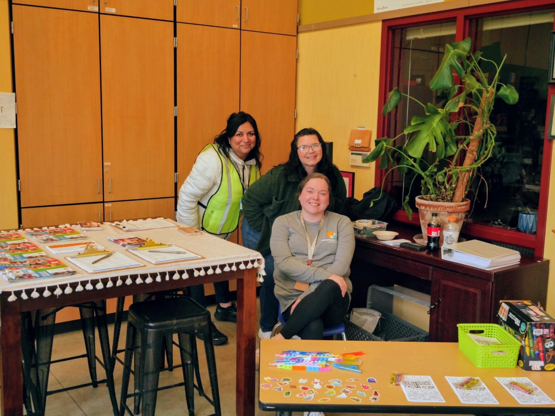 Three people sit behind a couple tables filled with swag to take home