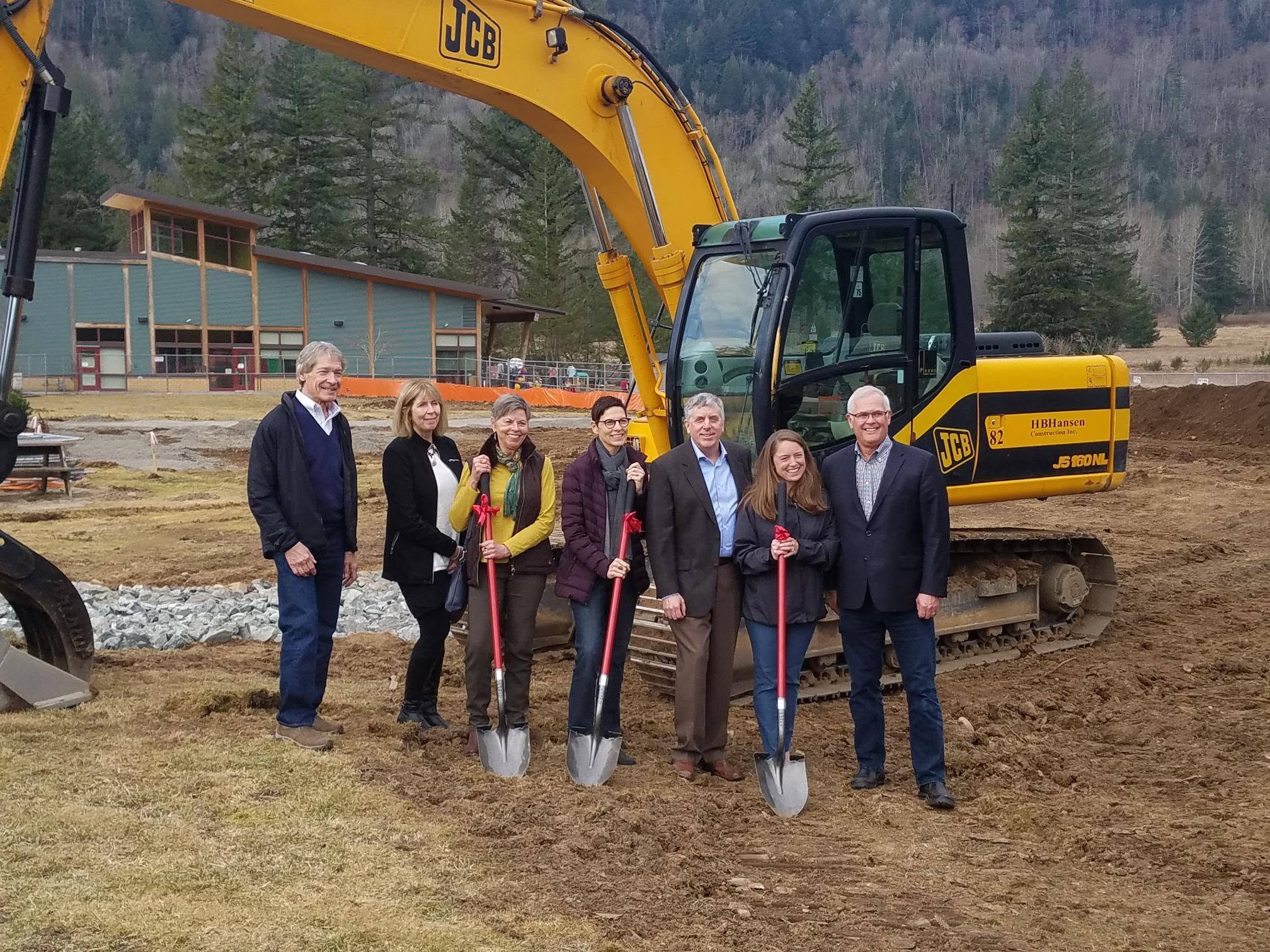 People stand in the dirt at a construction site holding golden shovels.