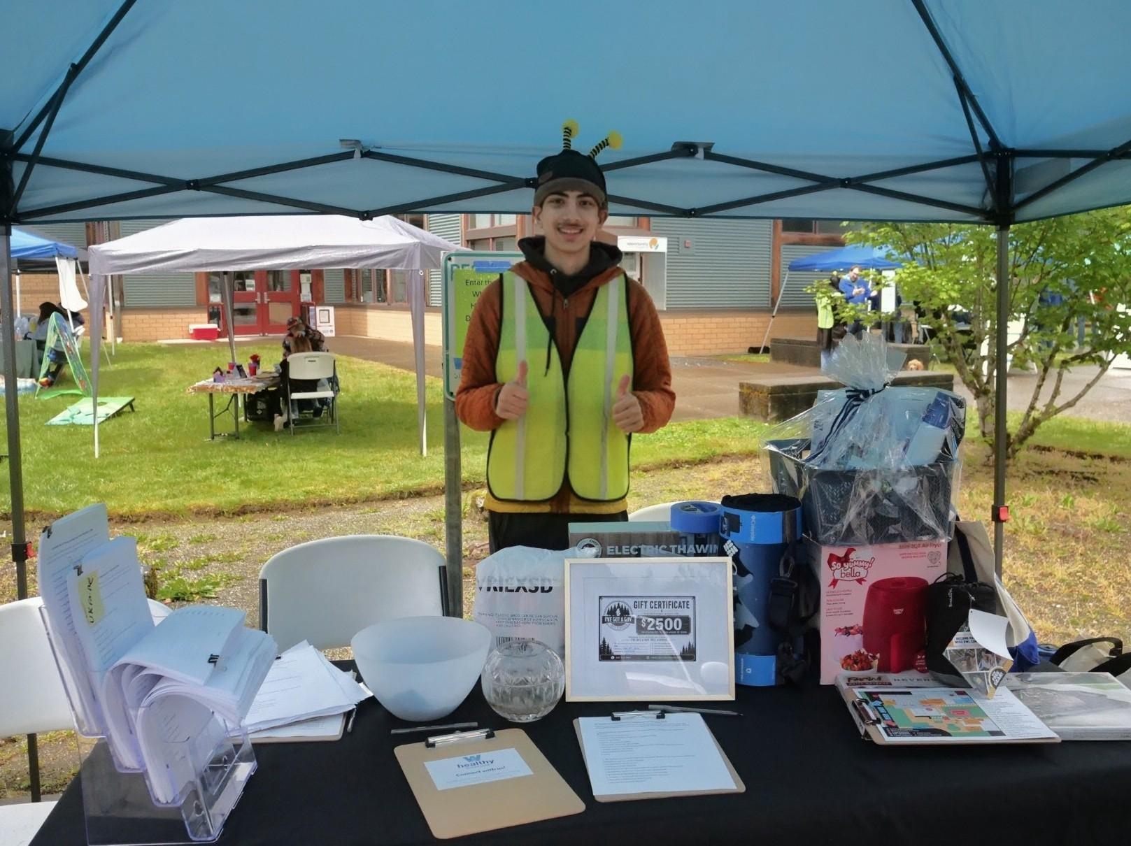 A person gives two thumbs-up under a canopy at an info table.