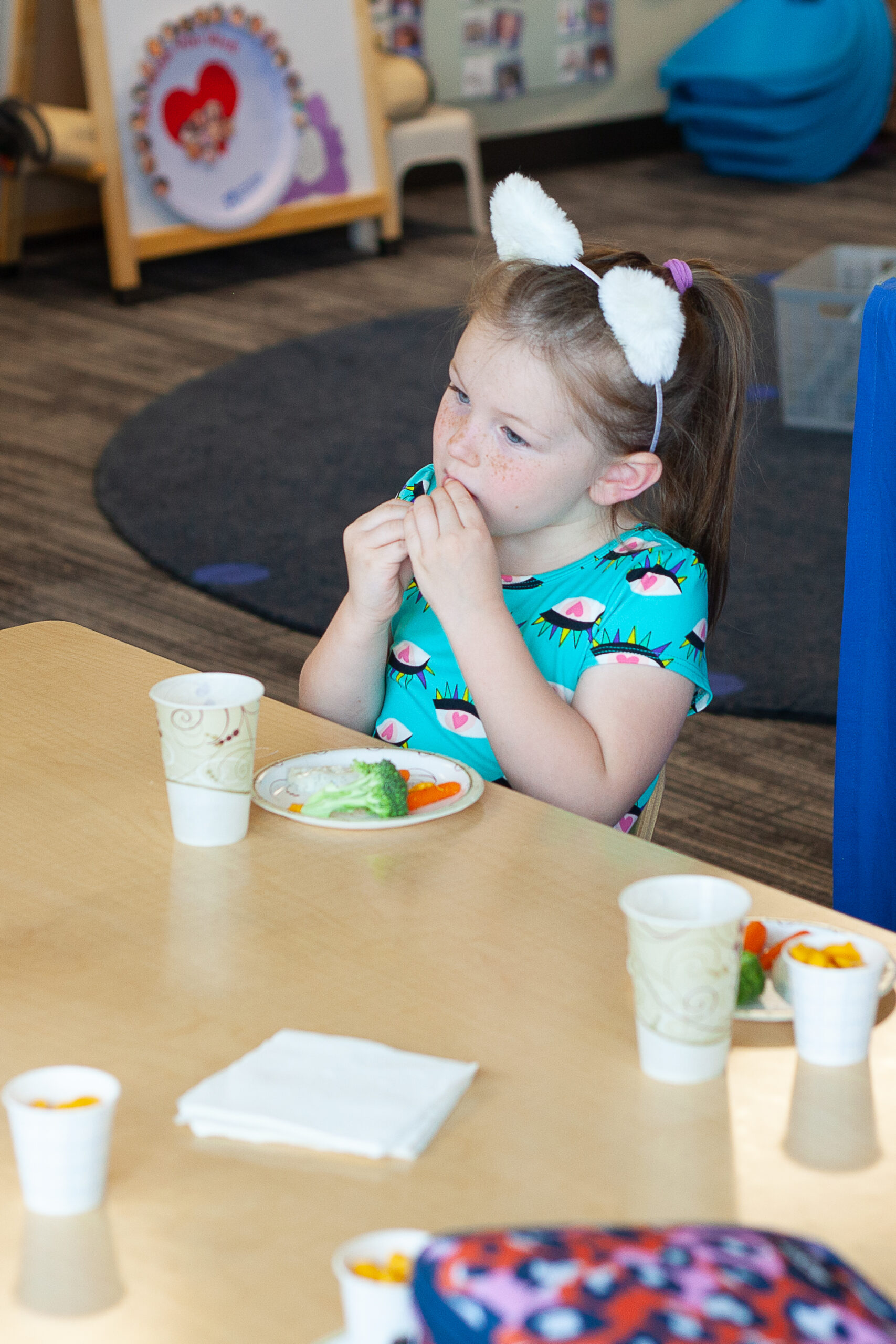 A little girl eats her vegetables at a table