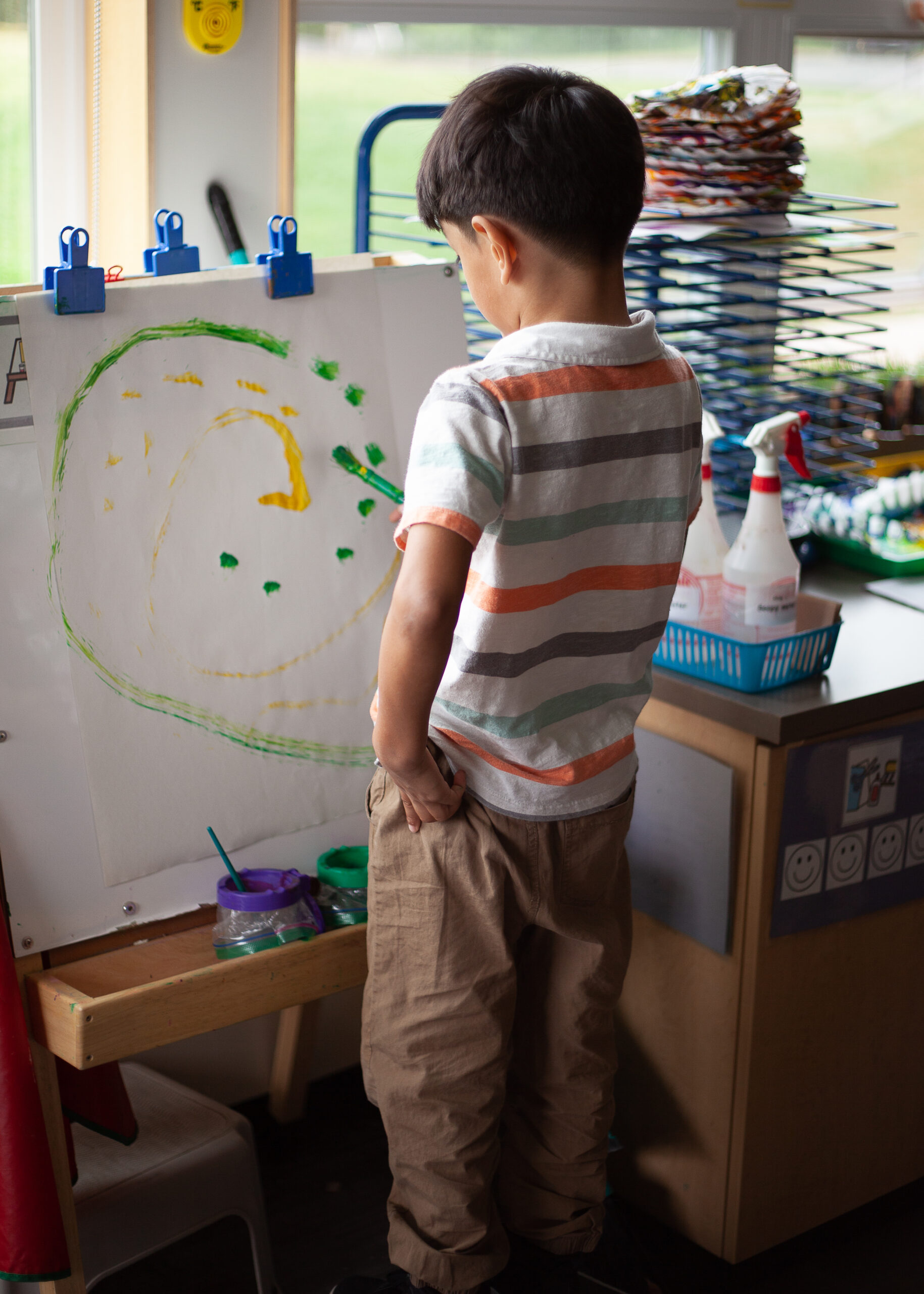 A boy paints a swirl of yellow and green on an easel